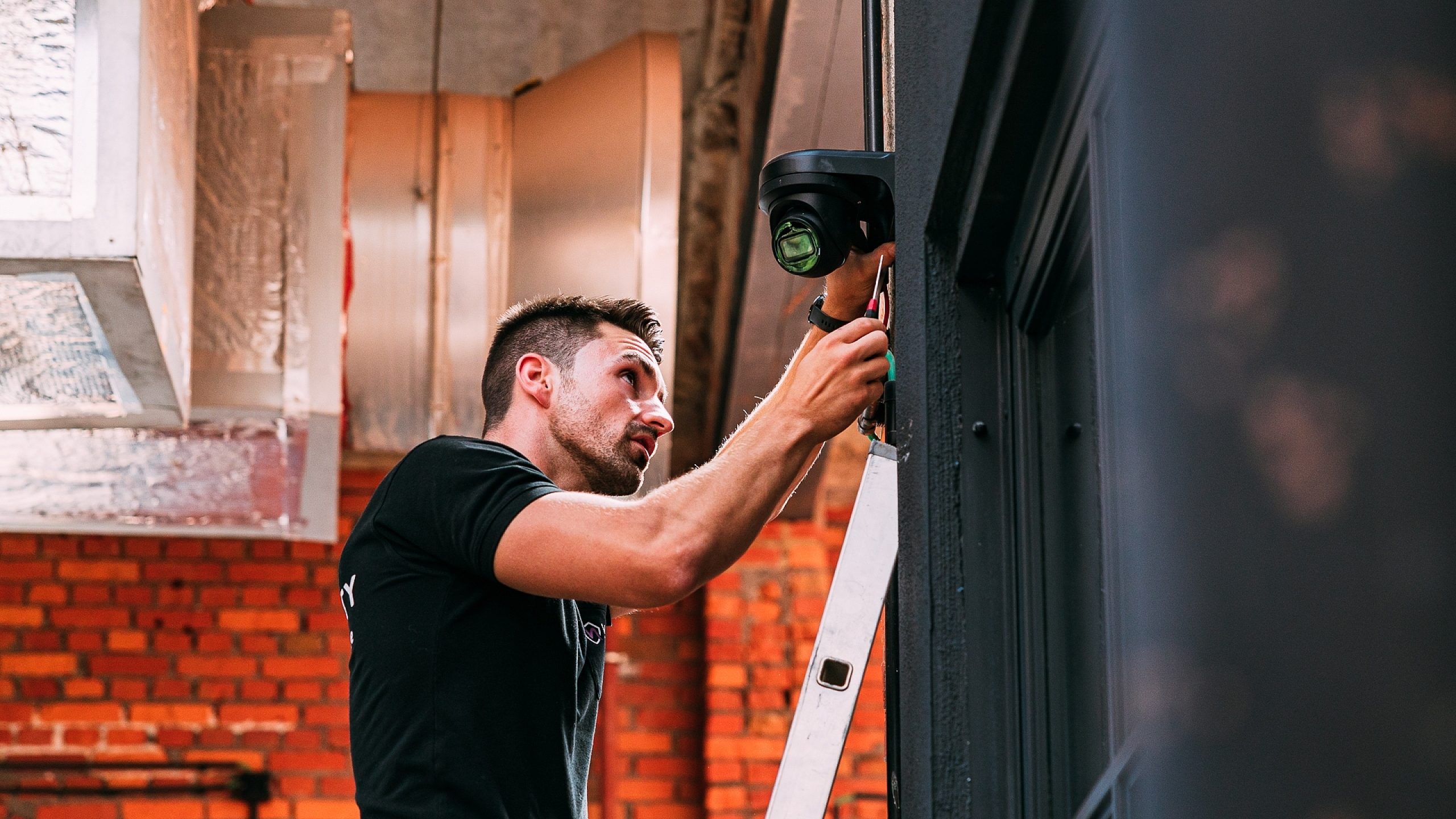 Beveiligingstechnieker op ladder plaatst camerabewaking bij bedrijf